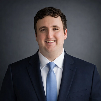 Timothy J. Singler in a blue suit, smiling, with a gray background.